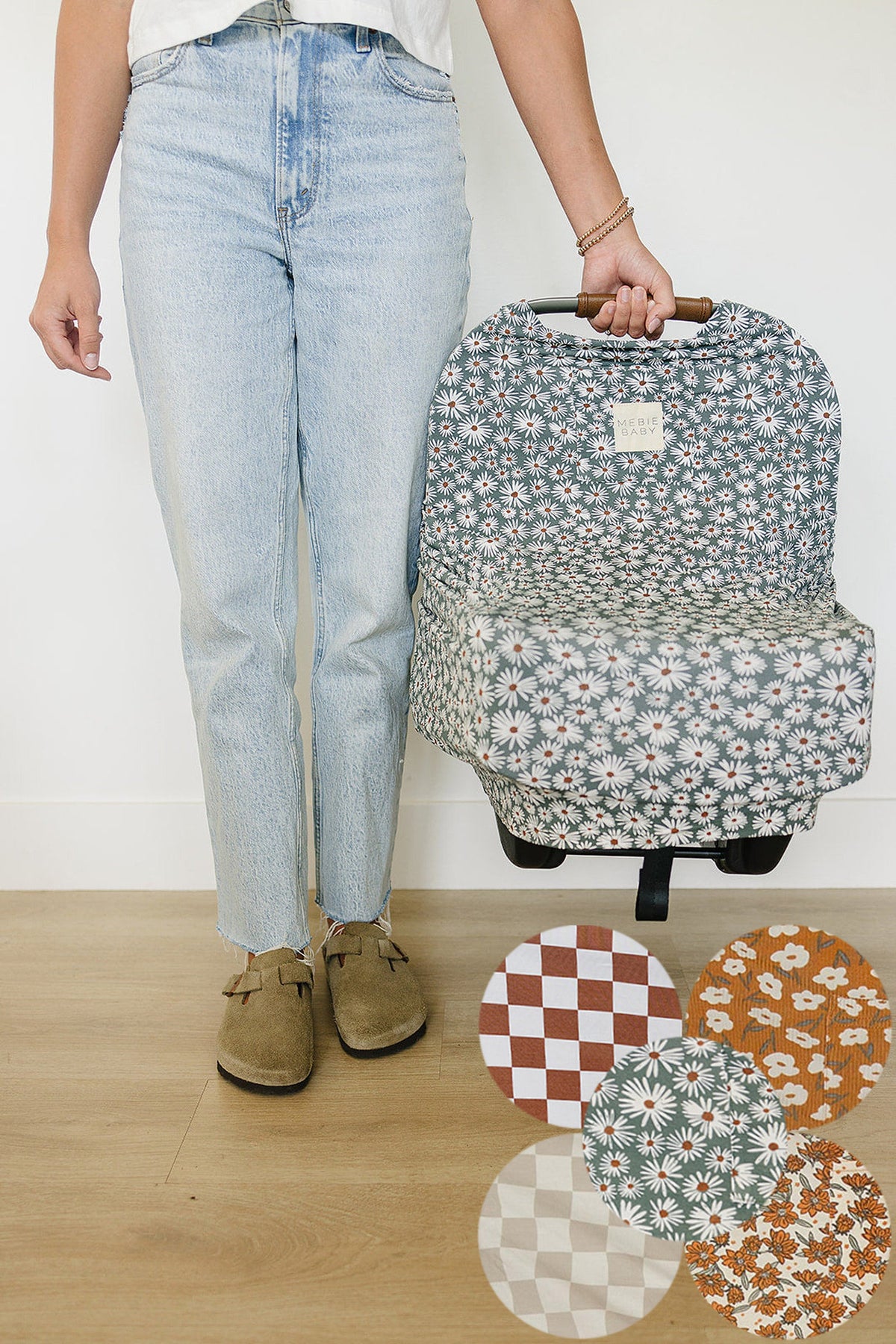 A person holds a floral-patterned Mebie Baby car seat cover. Five fabric swatches are displayed below.