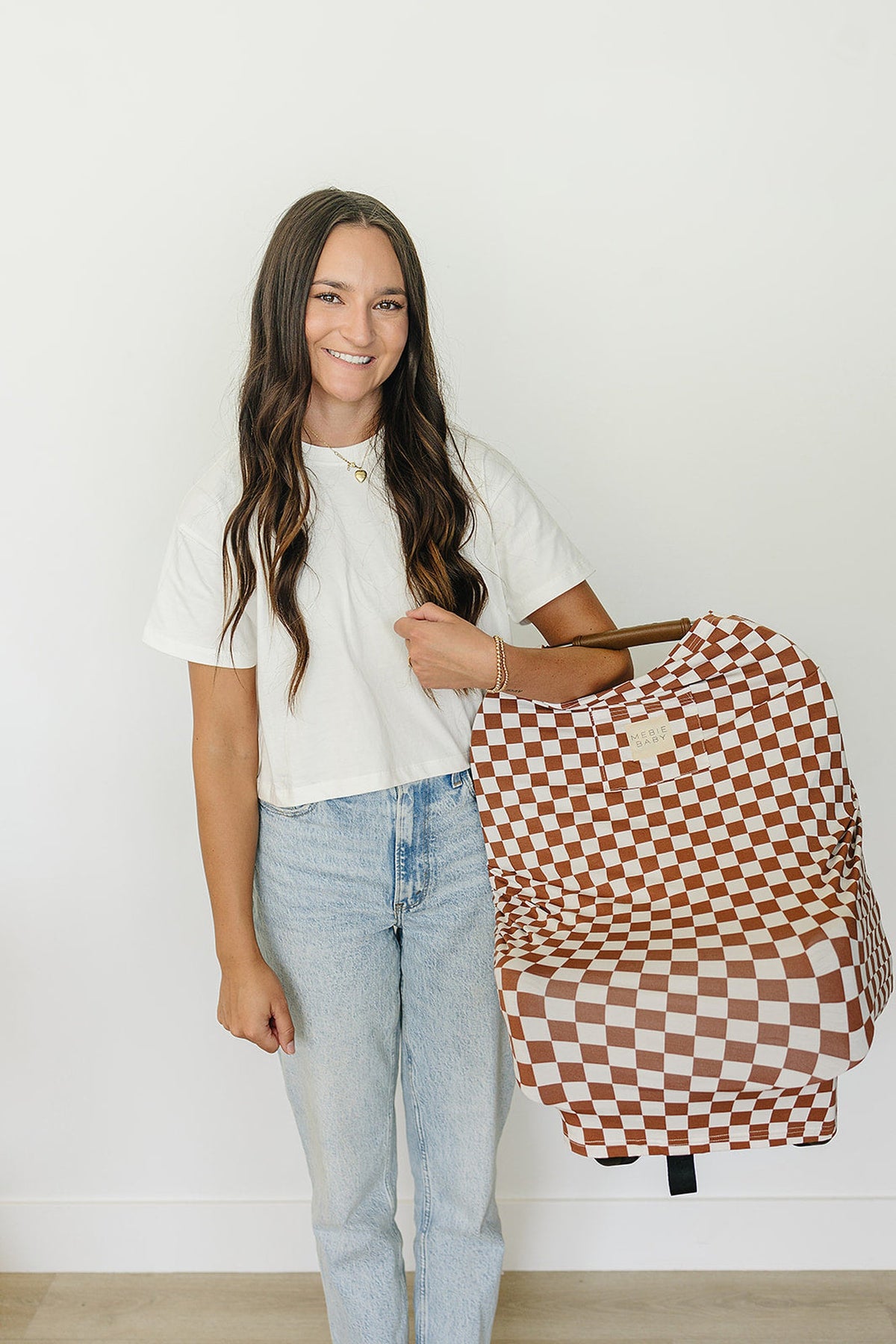 A woman in a white shirt holds a rust checkered multi-use bamboo cover against a plain background.
