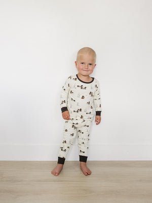 A toddler smiles while wearing a soft, ribbed bamboo pajama set with a playful animal print. The outfit features long sleeves and pants, perfect for cozy comfort day or night.
