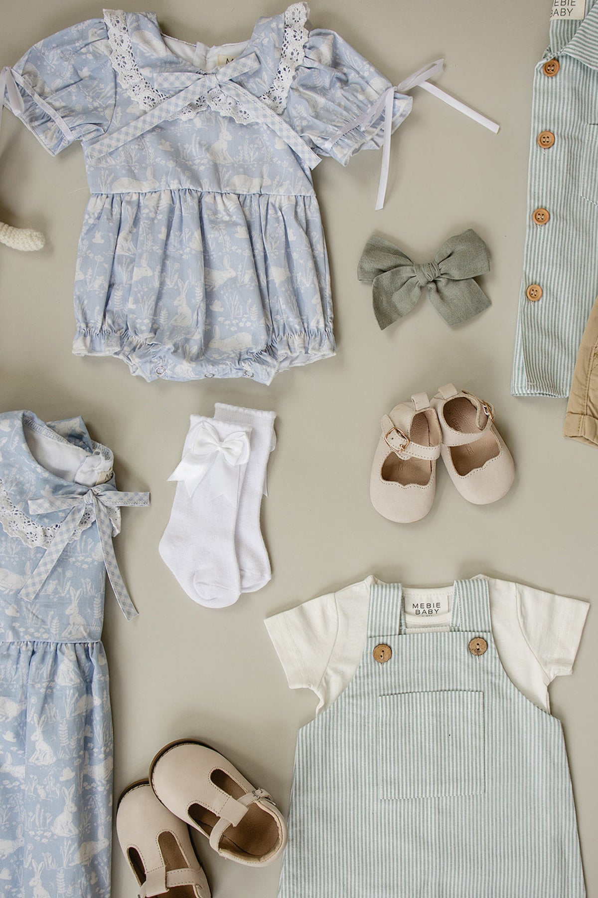 Baby clothes and accessories on display, including a blue dress, white socks with bows, and beige shoes.