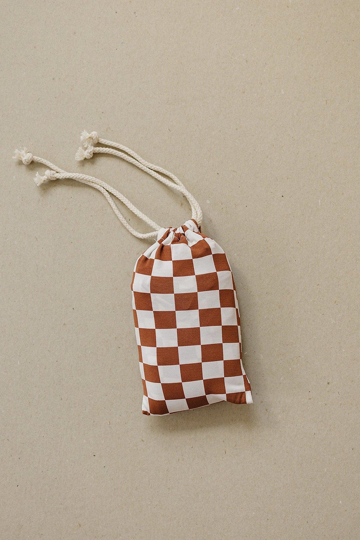 A drawstring pouch with a rust and white checkered pattern lies on a neutral surface.