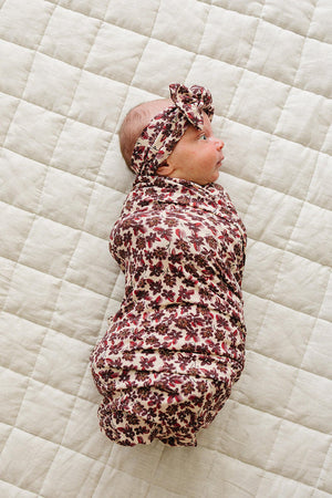 A newborn baby is swaddled in a floral ribbed bamboo stretch blanket, wearing a matching headband. The soft, breathable fabric features a delicate floral pattern against a neutral quilted background.