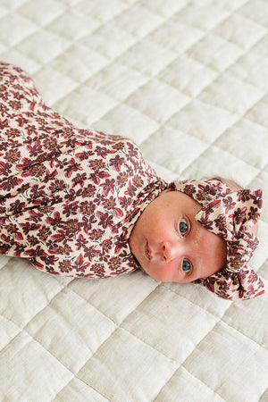 A baby wrapped in an antique floral ribbed bamboo swaddle lies on a textured, light-colored quilt. The swaddle features a soft, breathable fabric, ensuring comfort for delicate newborn skin.