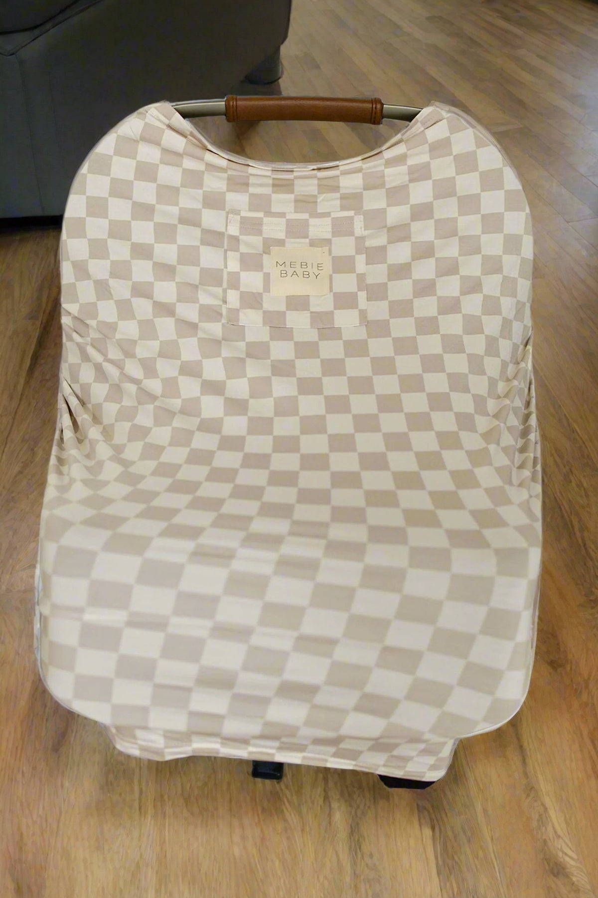 Taupe checkered car seat cover labeled Mebie Baby on a wooden floor, showcasing sustainable bamboo fabric.