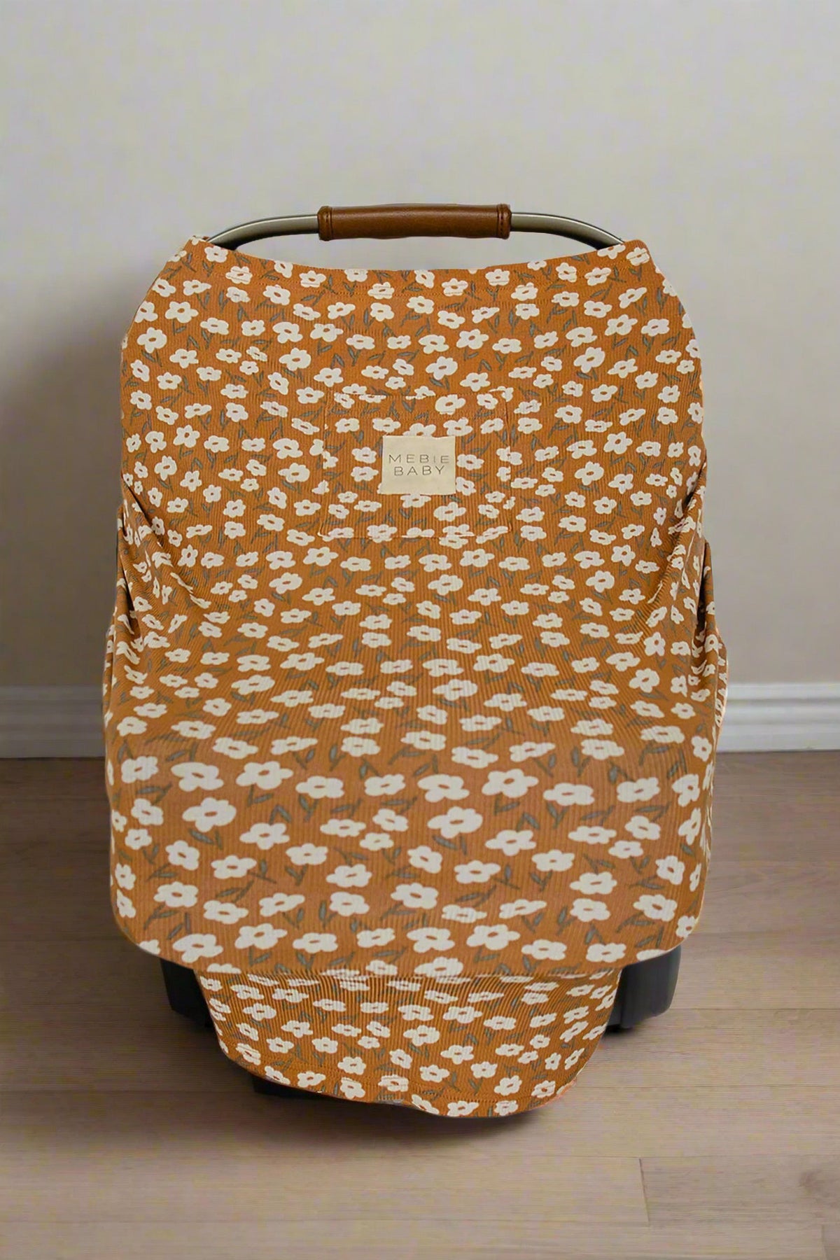 Mustard floral Mebie Baby cover on a car seat, featuring white flowers and bamboo fabric, in a room.