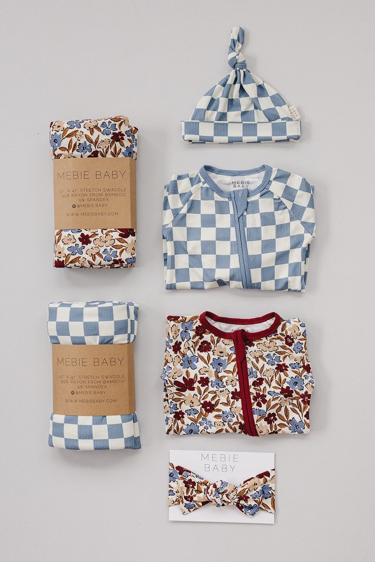 Blue checkered baby swaddle set with matching hat, floral clothing, and headband by Mebie Baby on a gray background.