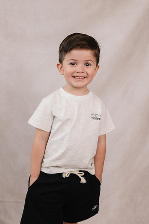 Young boy wearing a light gray T-shirt with a fish graphic and black shorts, smiling against a neutral background.