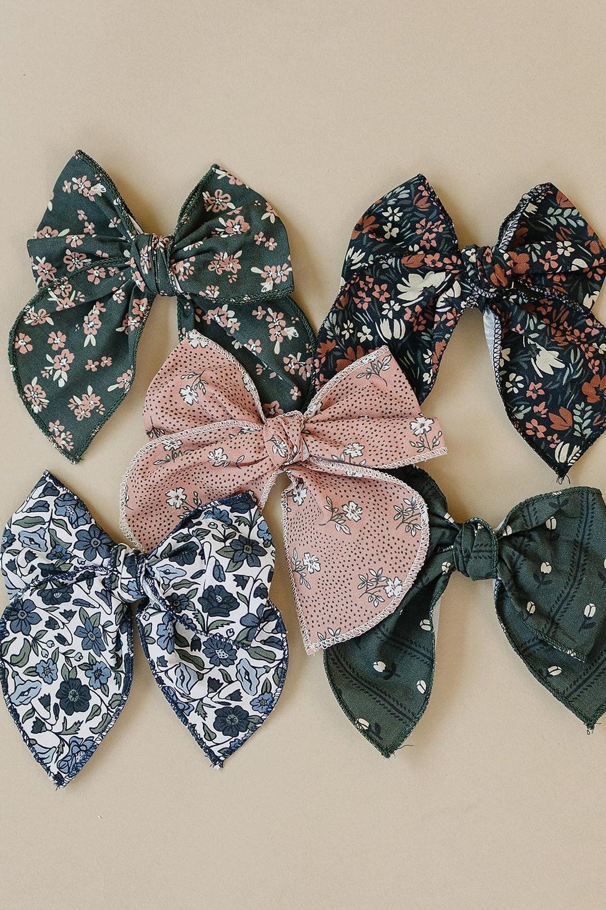 Five patterned fabric hair bows in floral and polka dot designs, featuring dark green, pink, and blue tones.