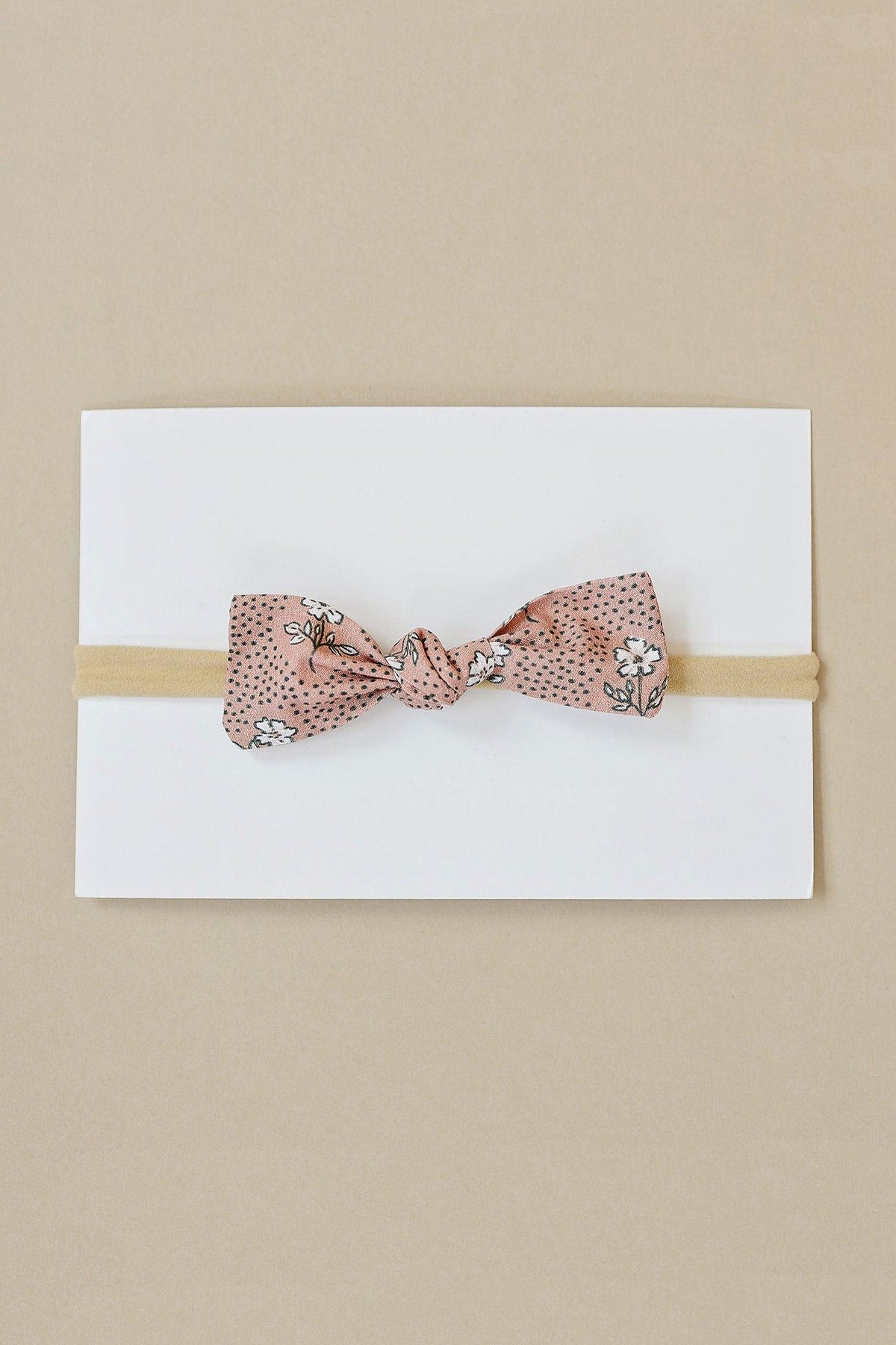 A pink floral cotton hair bow with a polka dot pattern on a beige elastic band, displayed on white card.
