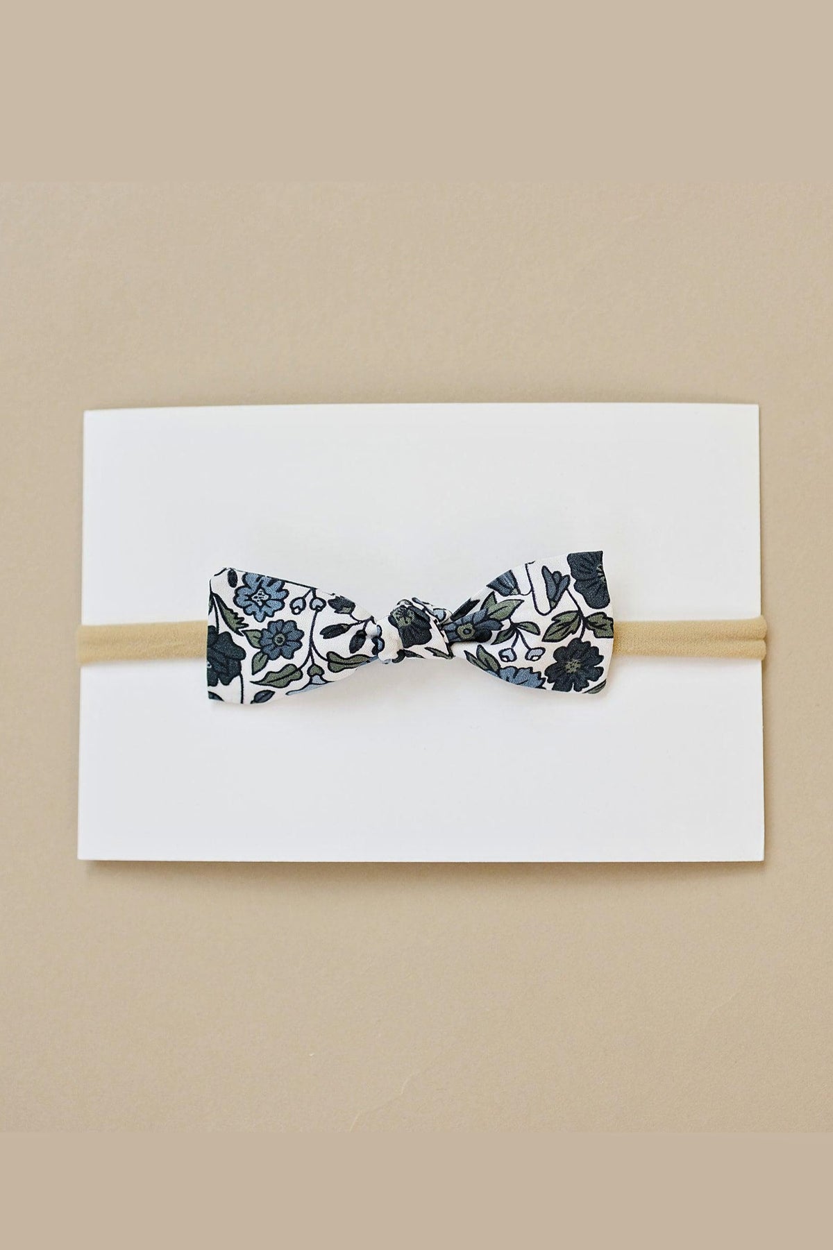 A floral-patterned bow with blue flowers on a tan elastic headband, set against a white background.
