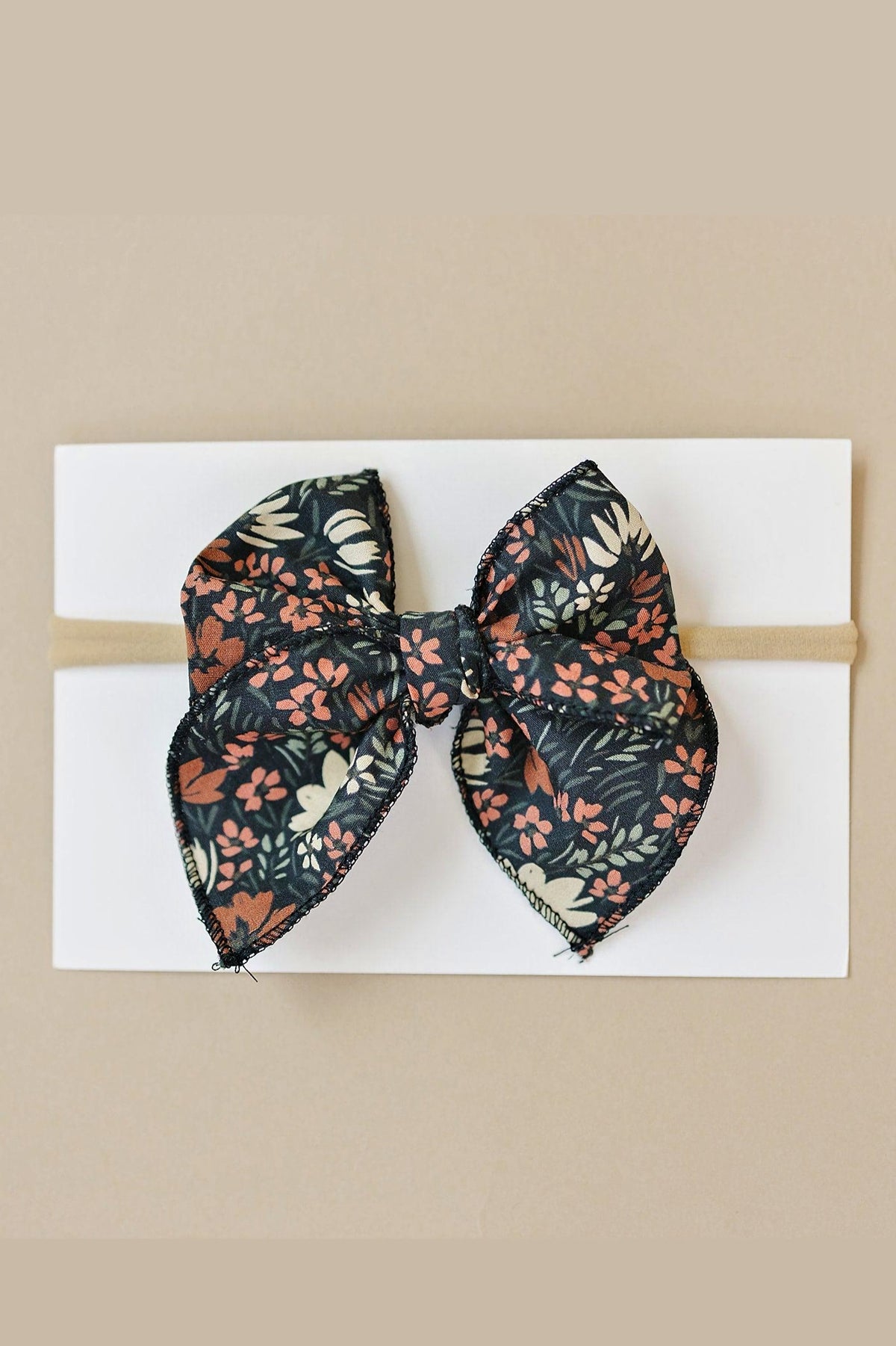 A floral patterned fabric hair bow on a white card, featuring pink and cream flowers on a dark background.