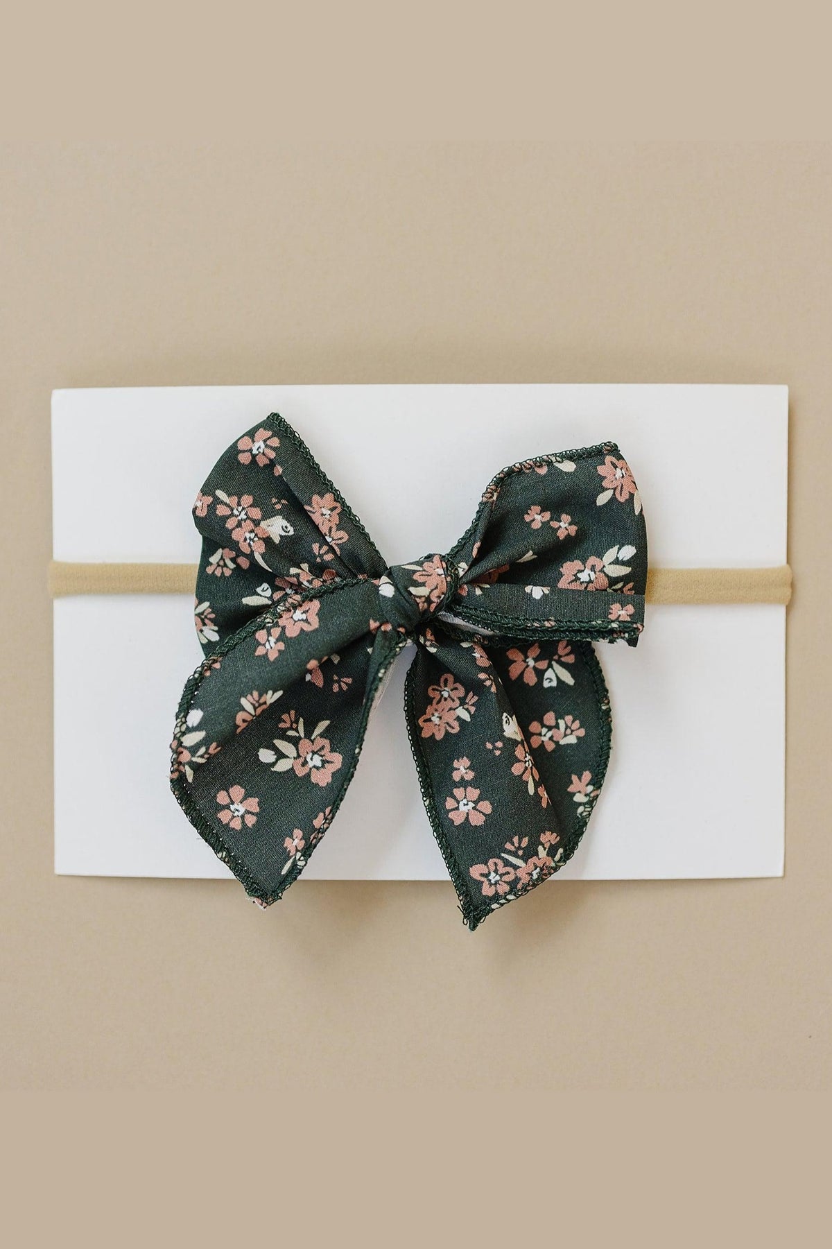 A floral-patterned fabric bow in dark green with pink flowers, displayed on a white card background.