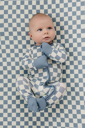 A baby in blue checkered pajamas lies on a matching checkered crib sheet, creating a cohesive, stylish look.