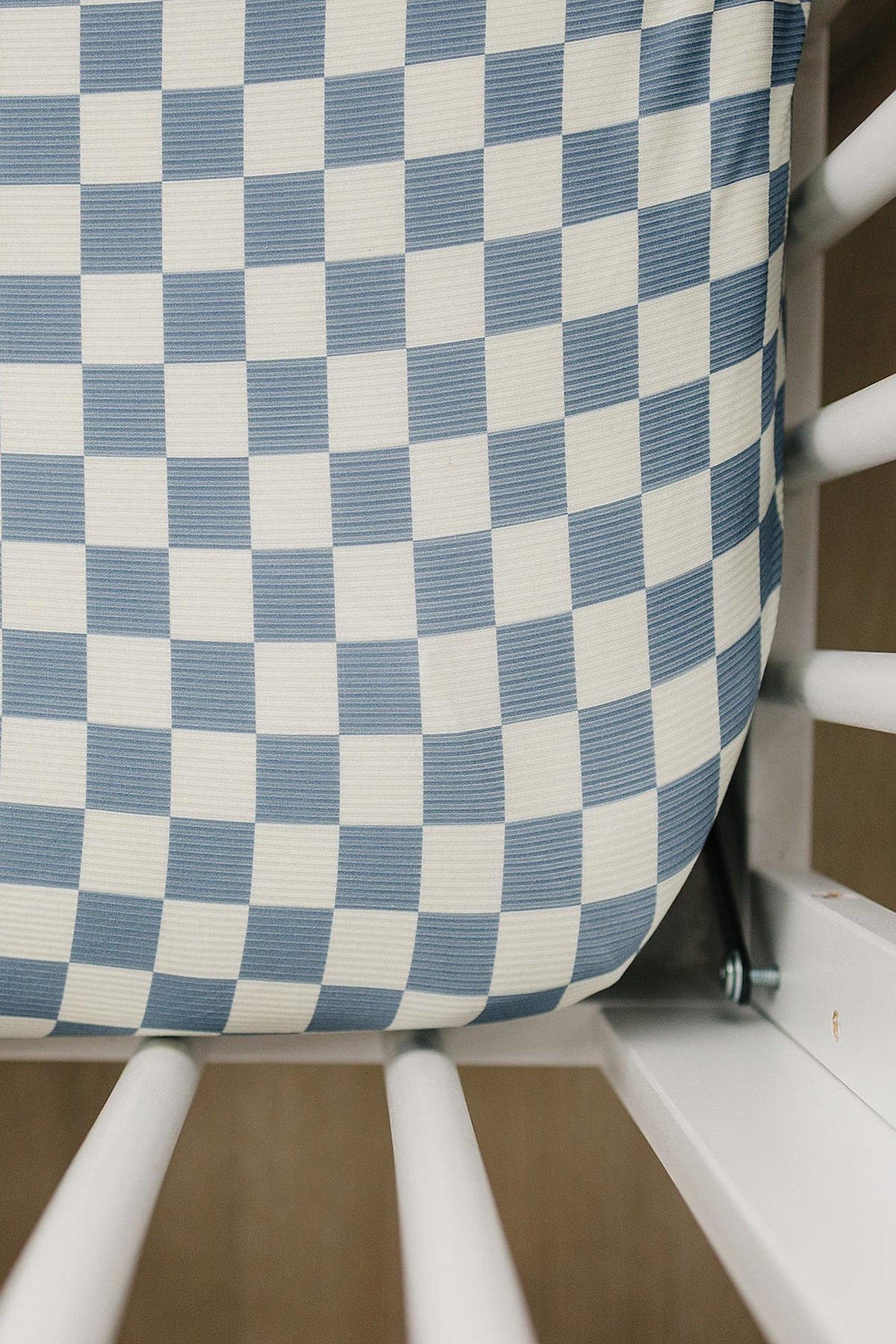 Blue checkered crib sheet made from ribbed bamboo fabric, fitted snugly in a white crib. Eco-friendly and stylish.