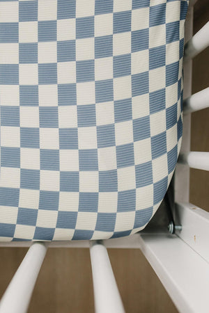 Blue checkered crib sheet made from ribbed bamboo fabric, fitted snugly in a white crib. Eco-friendly and stylish.