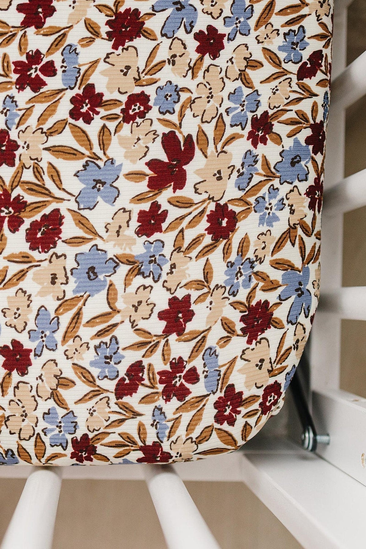 Floral crib sheet with red and blue flowers on ribbed fabric, fitted snugly on a white crib mattress.