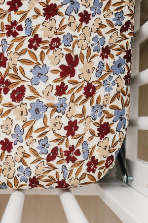 Floral crib sheet with red and blue flowers on ribbed fabric, fitted snugly on a white crib mattress.