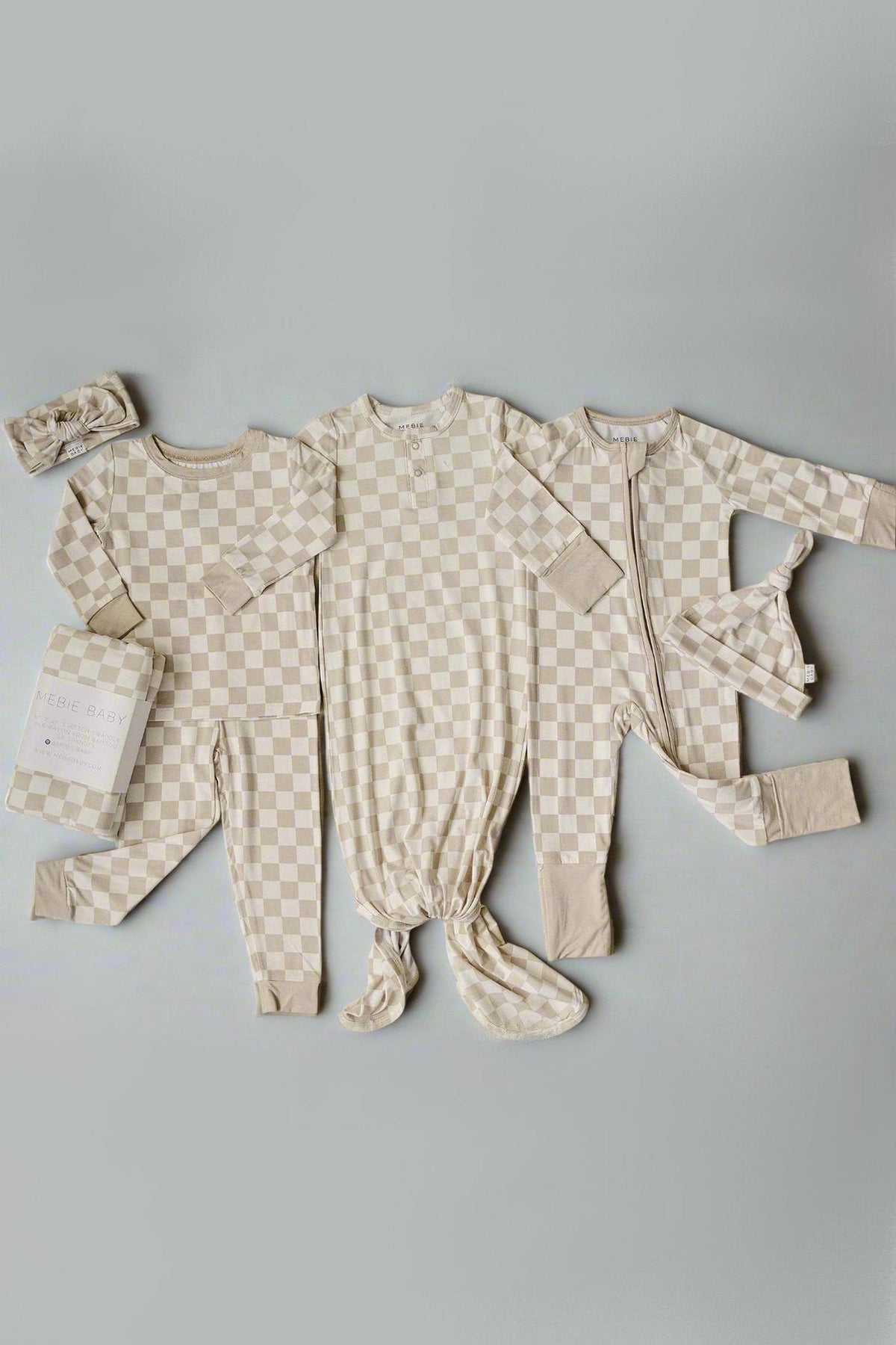 Taupe checkered baby outfits including pajamas, knotted gown, and headband, displayed on a neutral background.