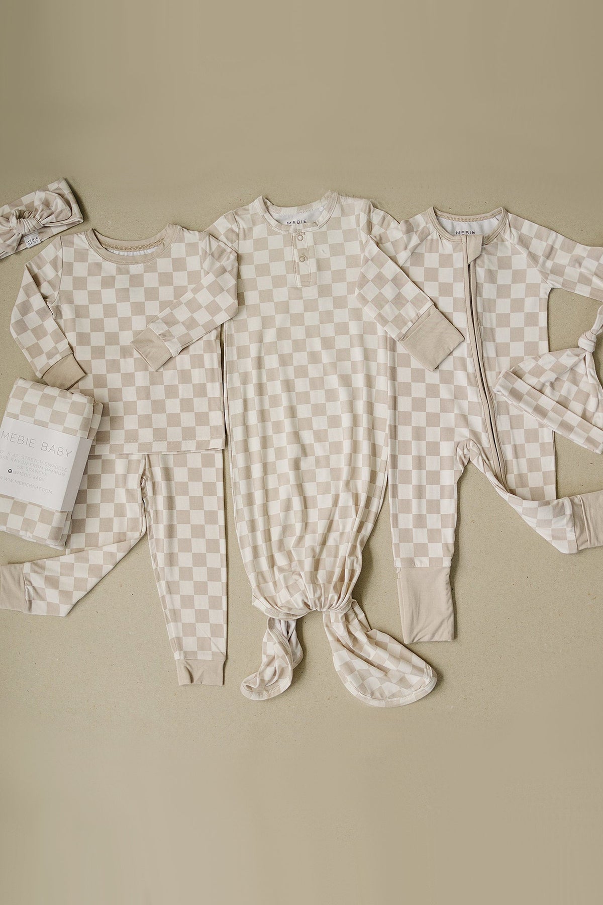 Three taupe checkered baby outfits, including pajamas and a knotted gown, displayed on a neutral background.