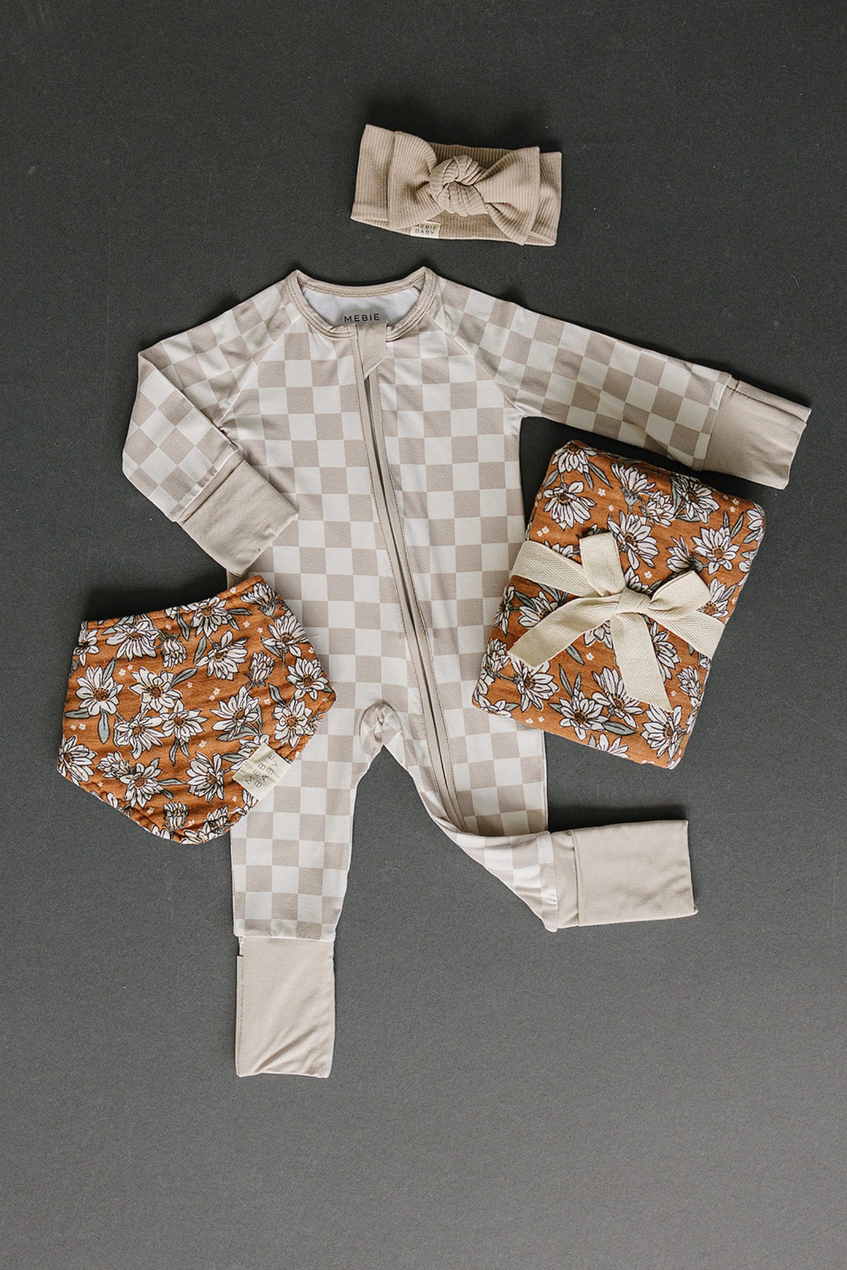 Taupe checkered baby pajama with a zipper, floral diaper cover, matching headband, and a floral blanket.