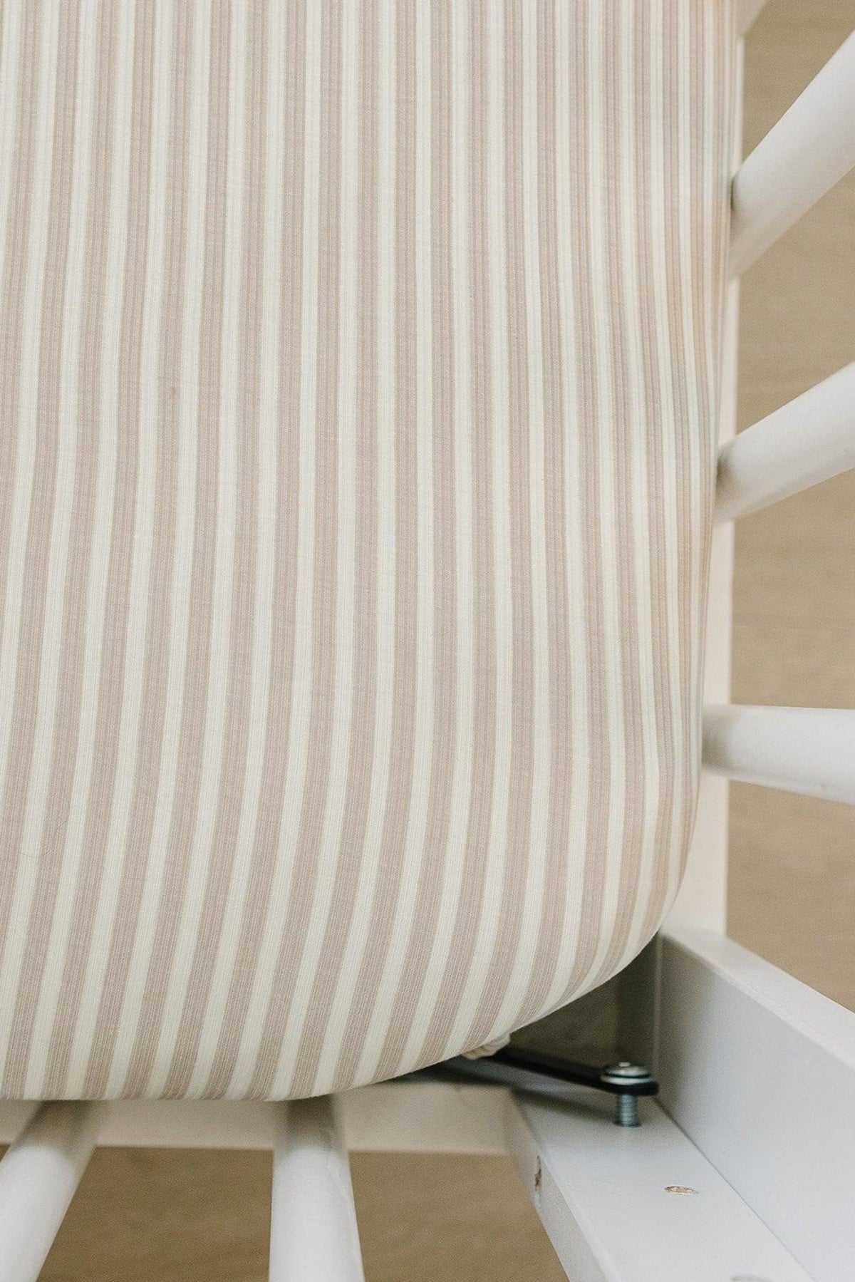 Close-up of a taupe striped ribbed crib sheet, made from soft bamboo fabric, fitting snugly on a white crib mattress.