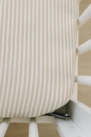 Close-up of a taupe striped ribbed crib sheet, made from soft bamboo fabric, fitting snugly on a white crib mattress.