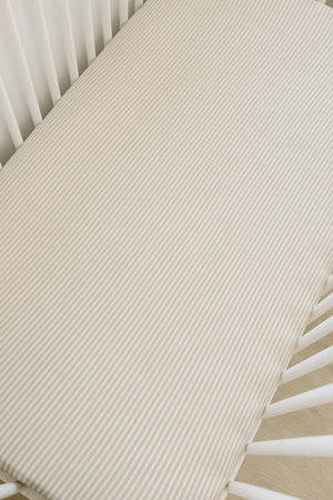 A taupe-striped ribbed crib sheet is neatly fitted onto a white crib mattress, showcasing soft, breathable bamboo fabric.