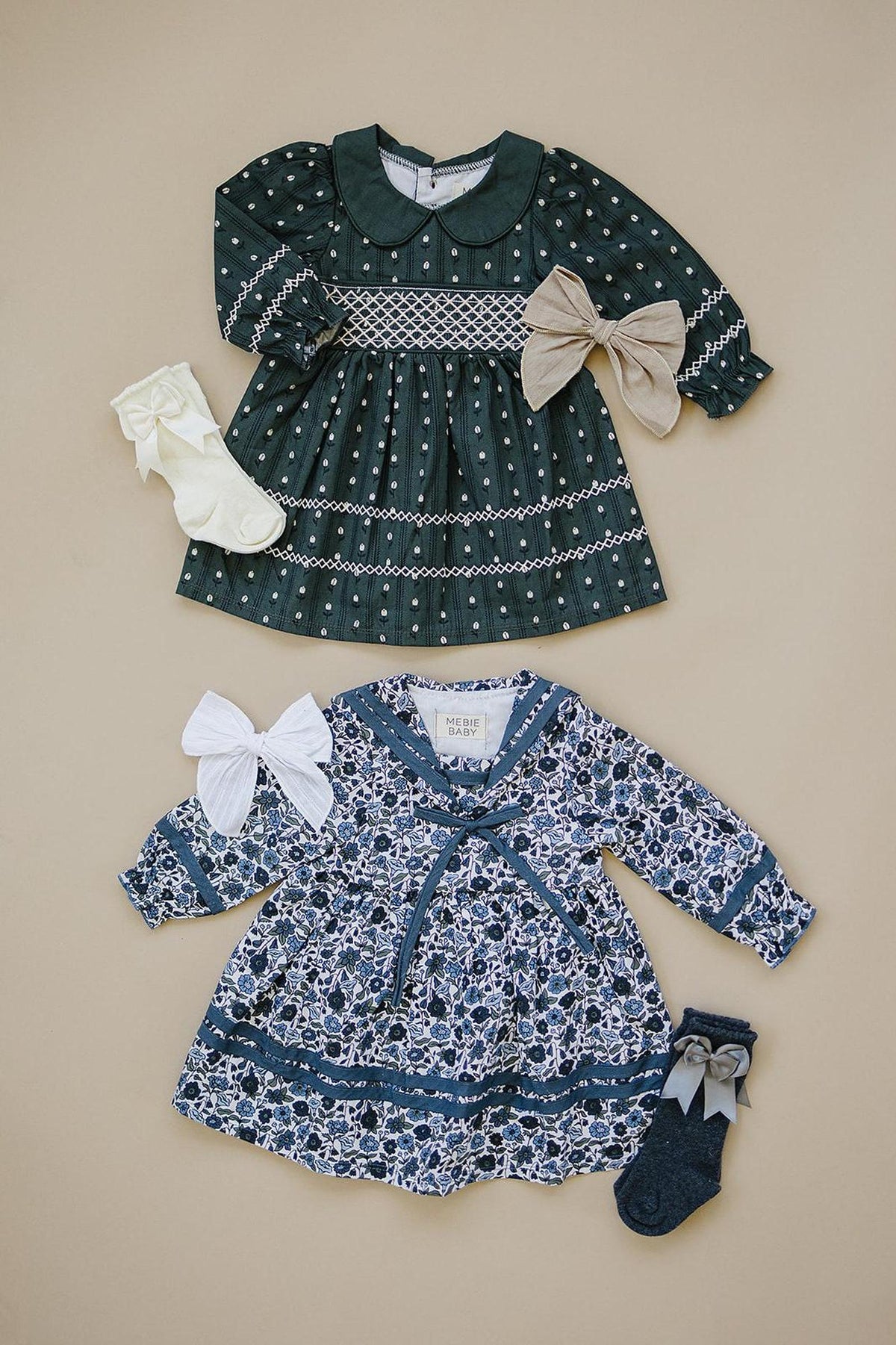 Two floral long-sleeve dresses with bows and matching socks on a beige background, featuring intricate patterns and collars.