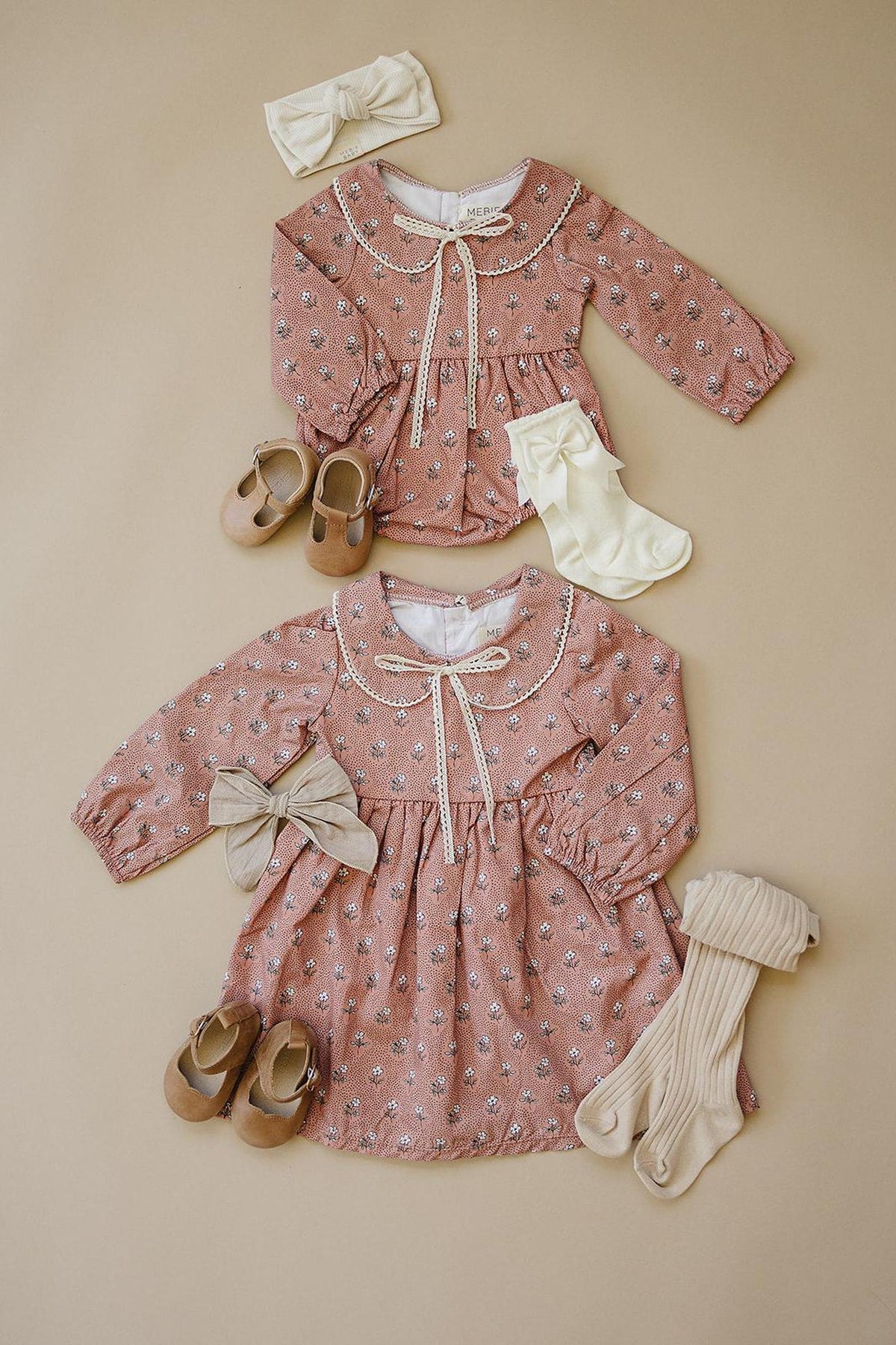 Two pink floral dresses with lace-edged collars, paired with bows, shoes, and socks on a beige background.