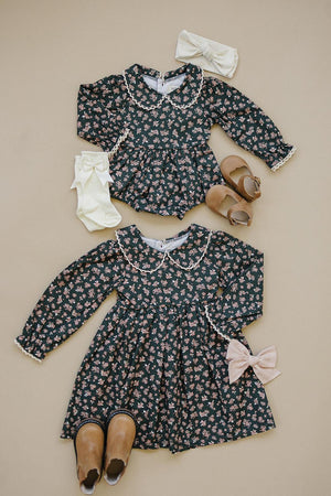 Two floral dresses with Peter Pan collars, matching shoes, bows, and socks on a beige background.