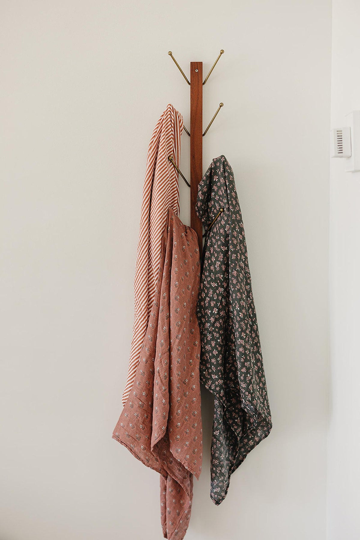 Three muslin blankets with striped and floral patterns hang on a wooden wall hook.