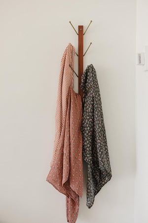 Three muslin blankets with striped and floral patterns hang on a wooden wall hook.