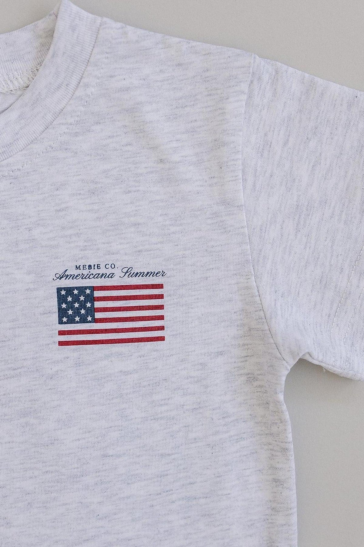White cotton T-shirt featuring a small American flag graphic and Mebie Co. Americana Summer text on the front.