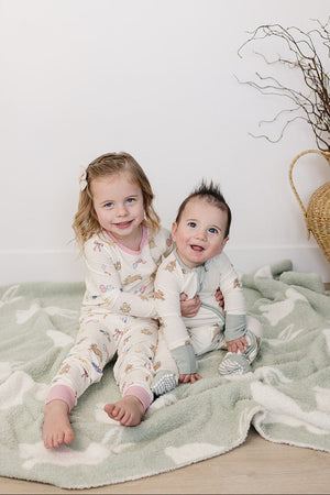 A girl and a baby sit on a soft, green blanket, wearing cozy pajama sets featuring playful bunny patterns.