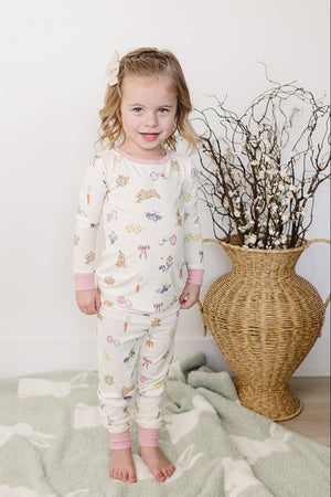 A young girl smiles while wearing a pastel-colored pajama set featuring playful bunny and floral patterns, standing on a soft.