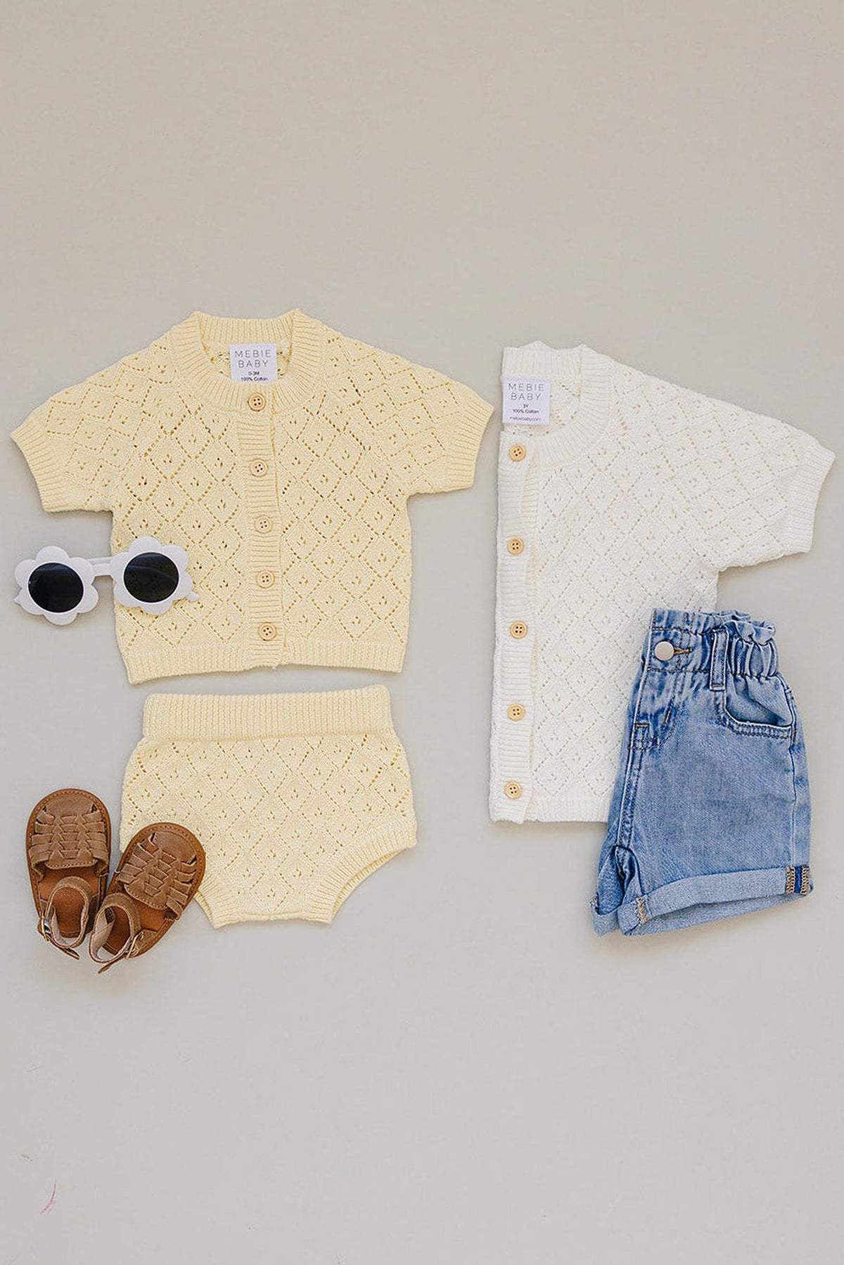A yellow and white knitted cardigan set for toddlers, paired with denim shorts and brown sandals, styled on a neutral.
