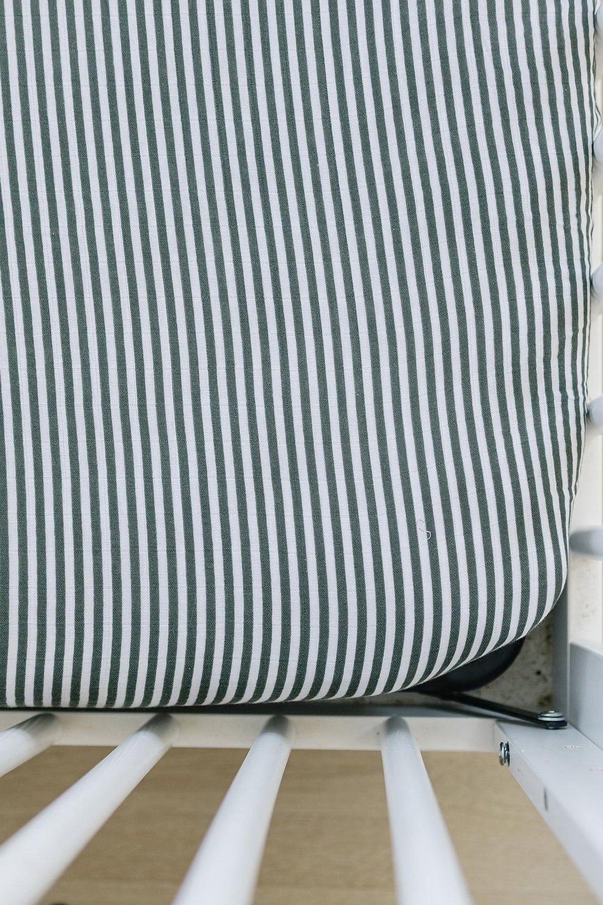 Green and white striped muslin crib sheet on a white crib. Made from soft, breathable 100% cotton fabric.