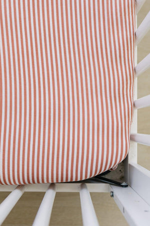 Pink and white striped muslin crib sheet covers a mattress within a white crib, showcasing a cozy design.