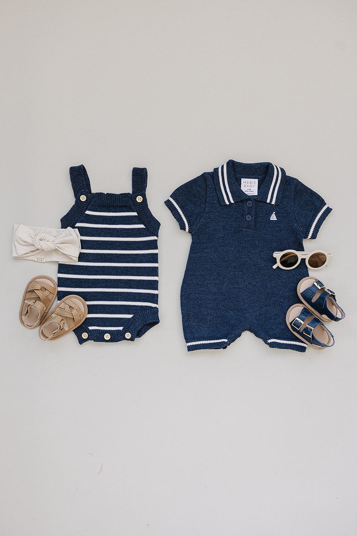 A navy and white striped knit bubble romper is displayed alongside a matching navy polo onesie, beige sandals, a headband, and sunglasses, showcasing a stylish, coordinated outfit for babies.