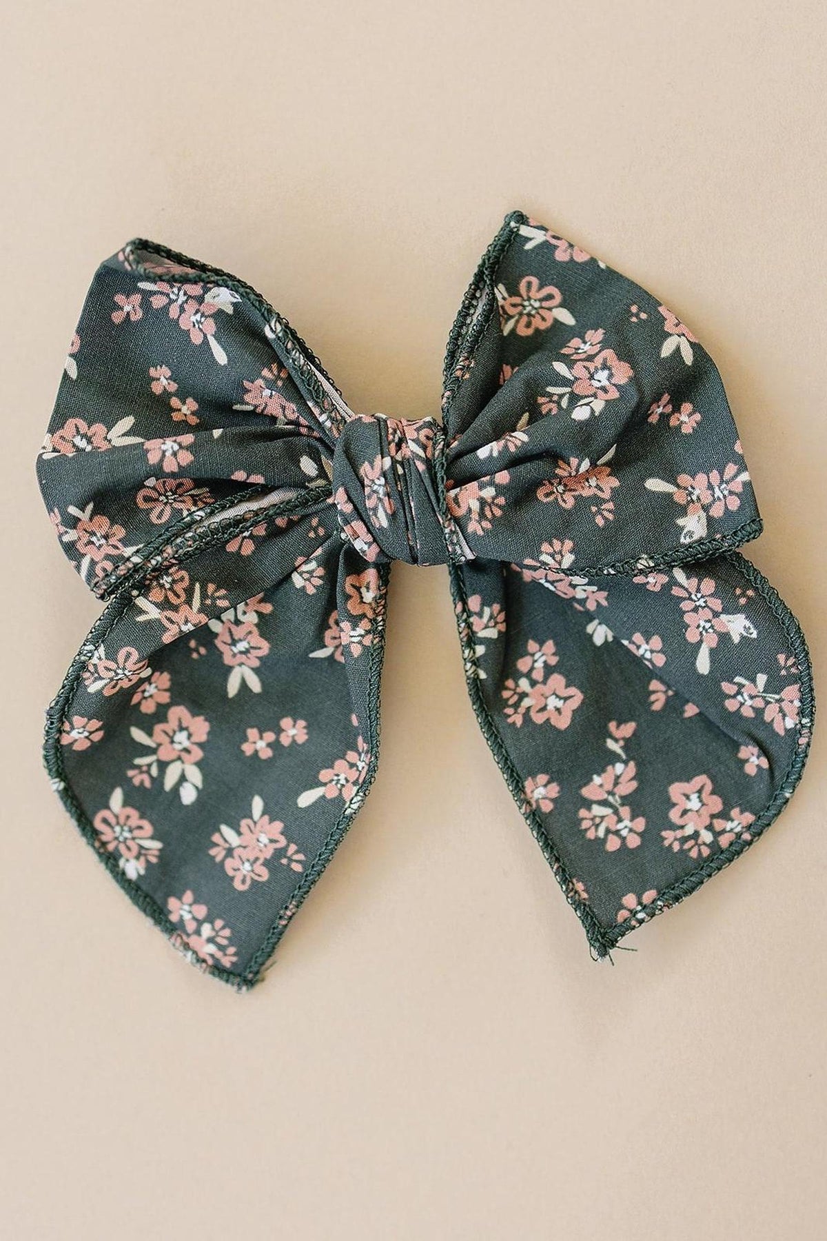 Dark green floral hair bow with pink and white flowers on a neutral background, crafted from soft fabric.