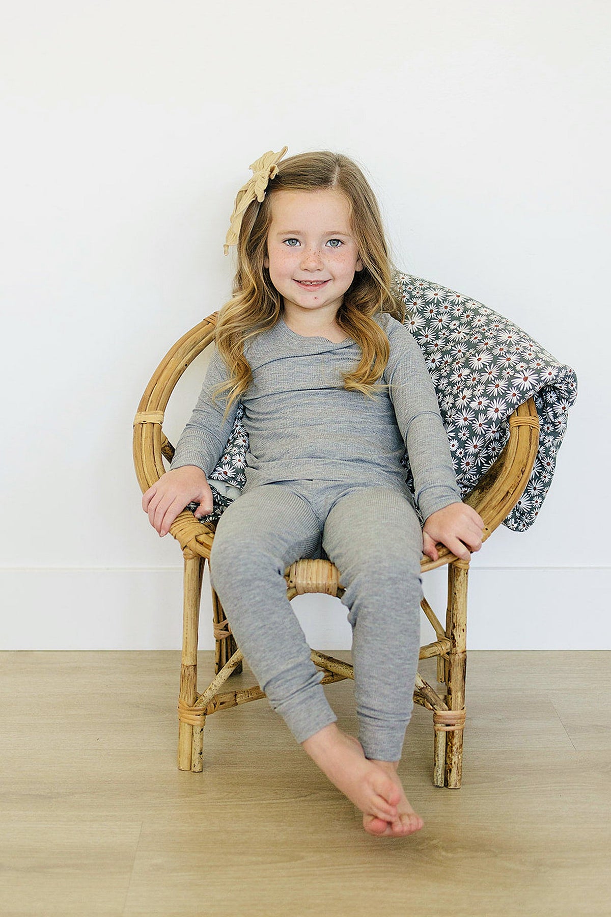 A child in a heather grey ribbed pajama set sits on a wooden chair with a floral blanket.
