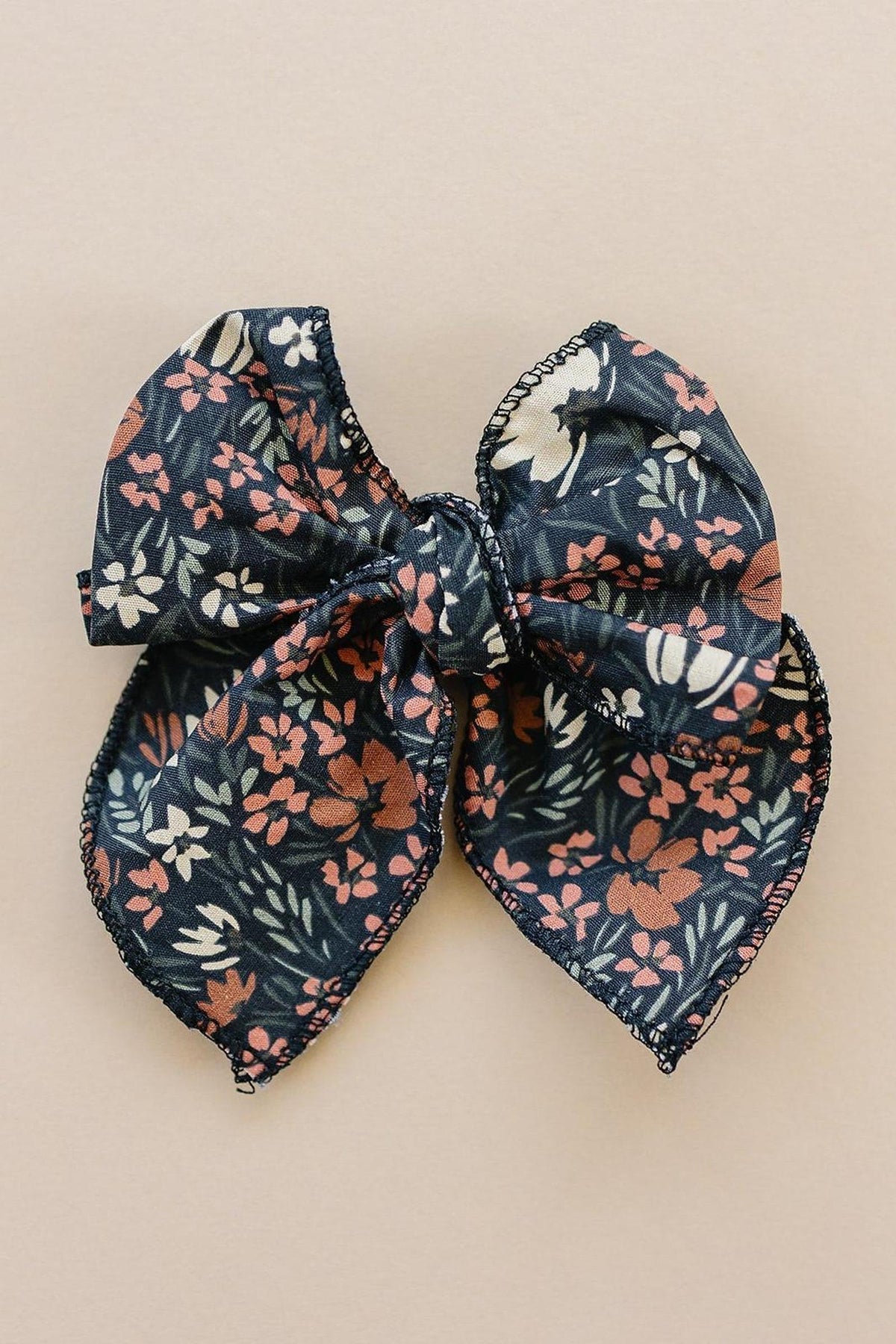 A navy floral-patterned fabric bow with pink and white flowers on a neutral beige background.