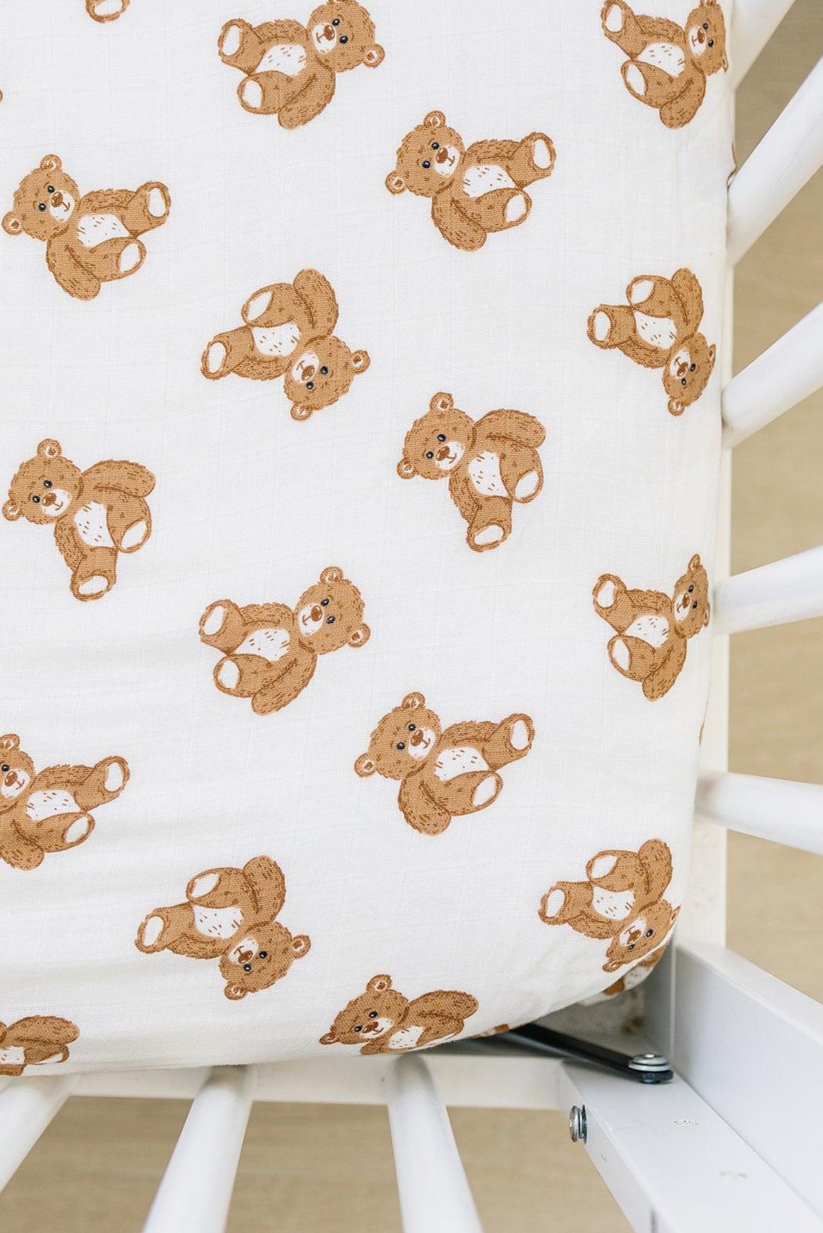 White muslin crib sheet with brown teddy bear pattern on a crib corner, showcasing soft cotton material.