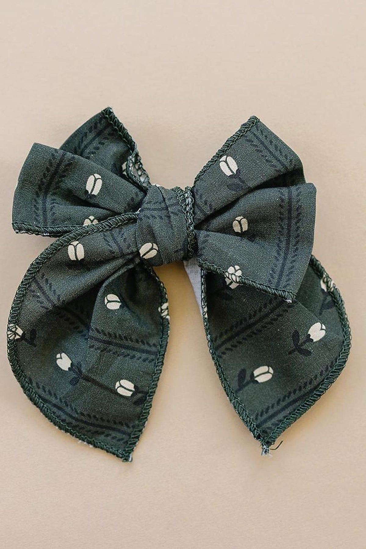 Dark green fabric bow with white floral patterns on a beige background, showcasing a chic, handcrafted design.