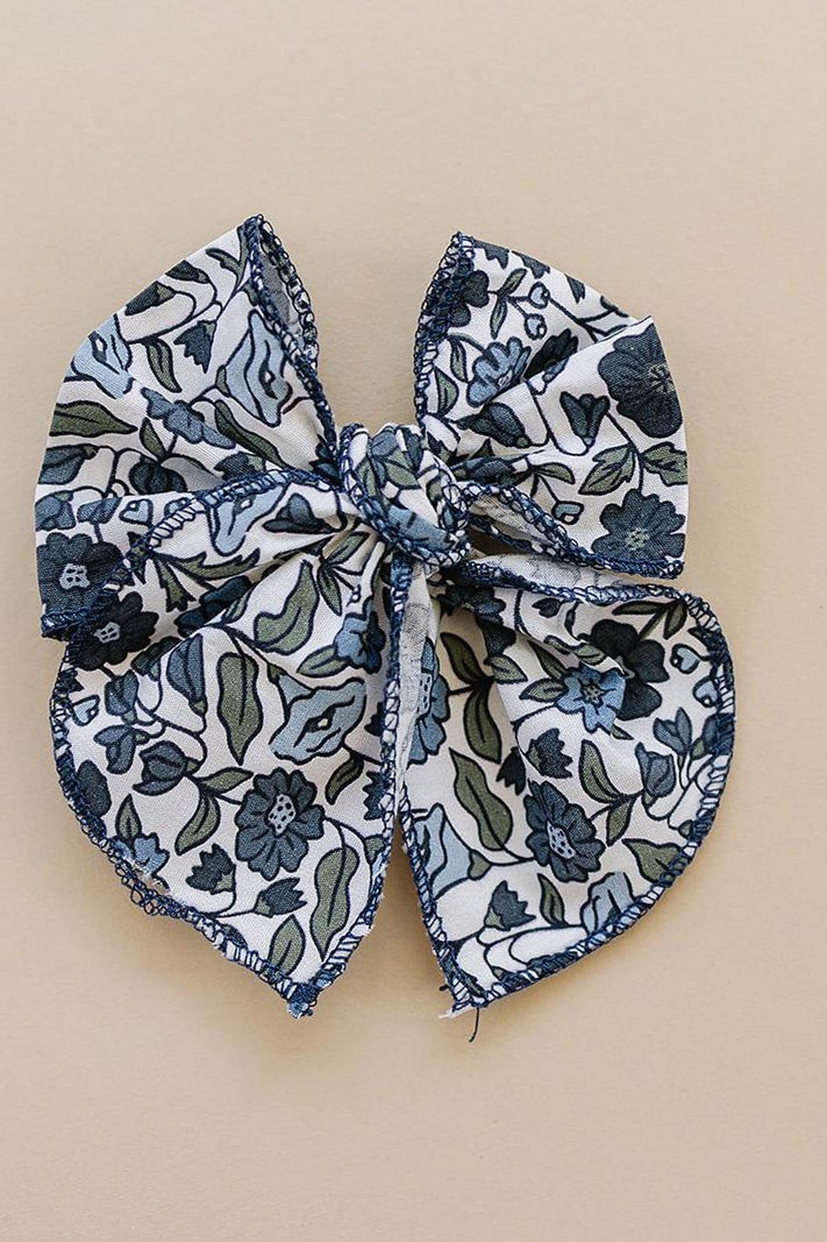 Floral-patterned fabric bow with blue and green designs on a beige background, featuring detailed stitching.