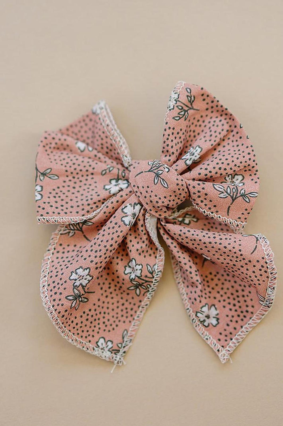 A pink floral-patterned cotton hair bow with black dots and white flowers, set against a beige background.