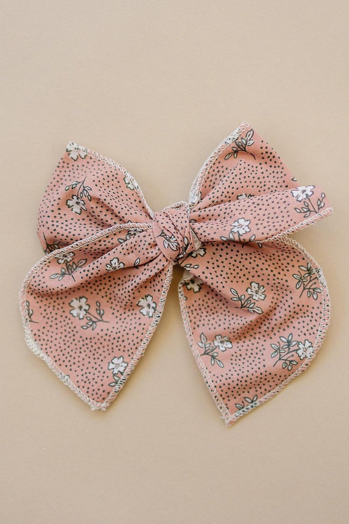 A pink floral fabric bow with white flowers and black dots, laid on a beige background.