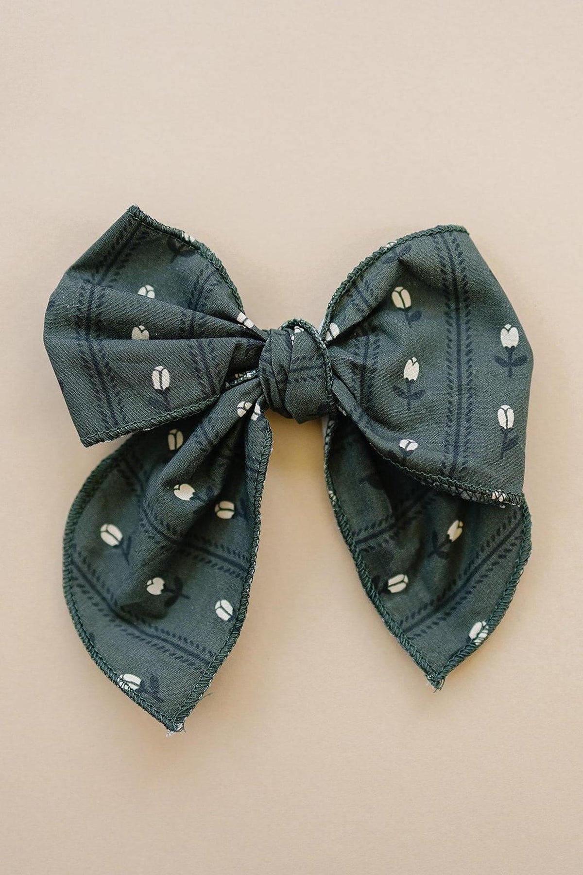Dark green fabric bow with a floral pattern on a beige background, suitable for babies and toddlers.