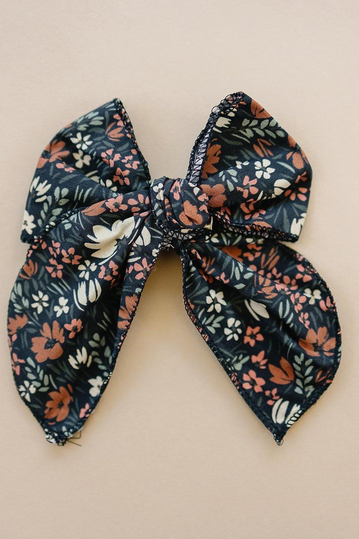 A floral fabric bow with a navy background and orange, white, and green accents on a beige surface.