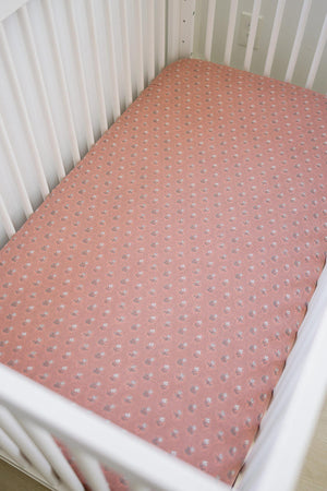 A white crib with a vintage pink floral muslin crib sheet, featuring small delicate patterns and soft fabric.